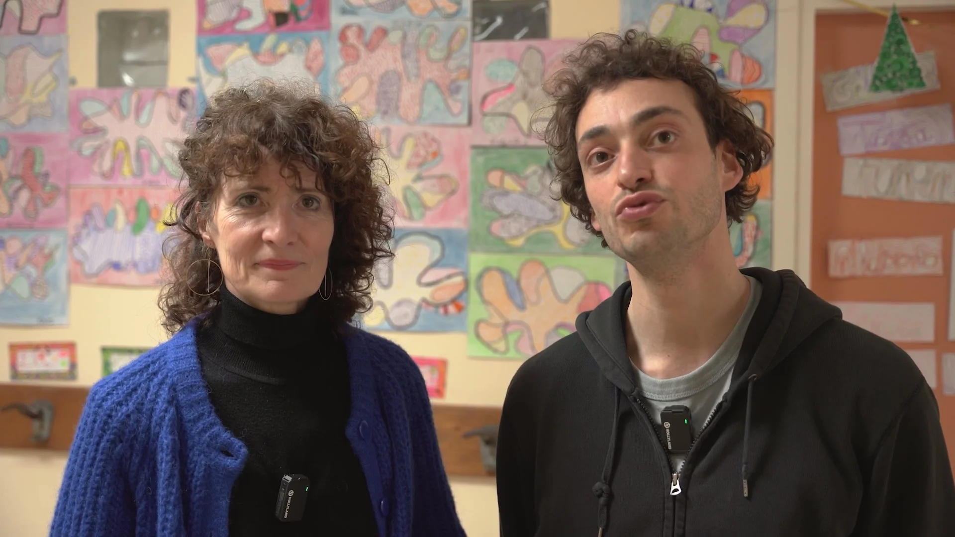 Béatrice et Samy devant un mur de dessins d'enfants après une représentation