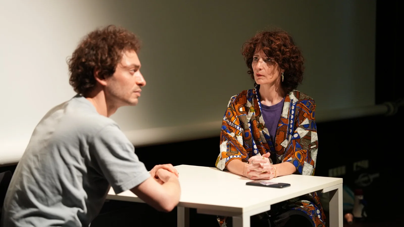 Samy et Béatrice assis face à face à la table dans une scène d'échange intense